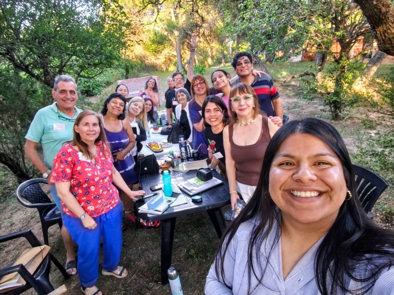 Selfie de un grupo alrededor de una mesa al aire libre con libros, mate y cuadernos.